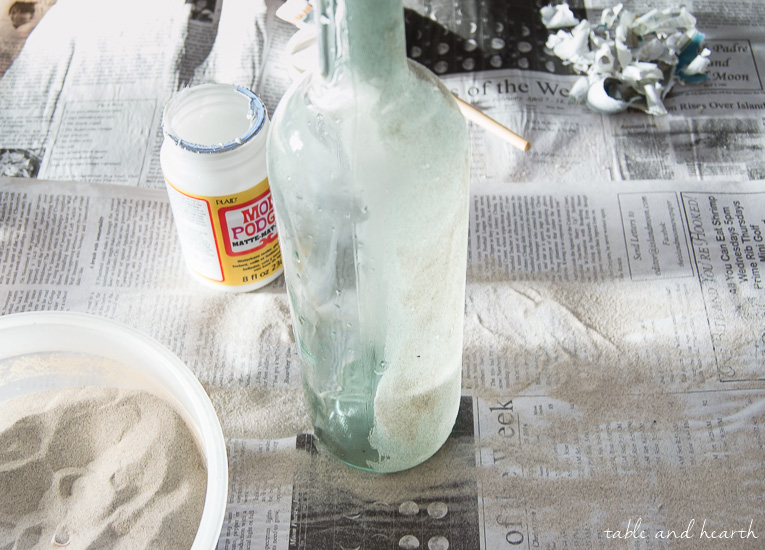 Who knew you could Mod Podge sand?! These beachy sand covered bottles are quick and easy to make with just some sand, Mod Podge, and empty bottles!